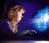 Little,Blond,Girl,Working,On,Computer,In,Dark,Room,At